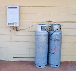 Picture of two LPG cylinders installed on a concrete slab, next to a house and connected to an instantaneous gas water heater.